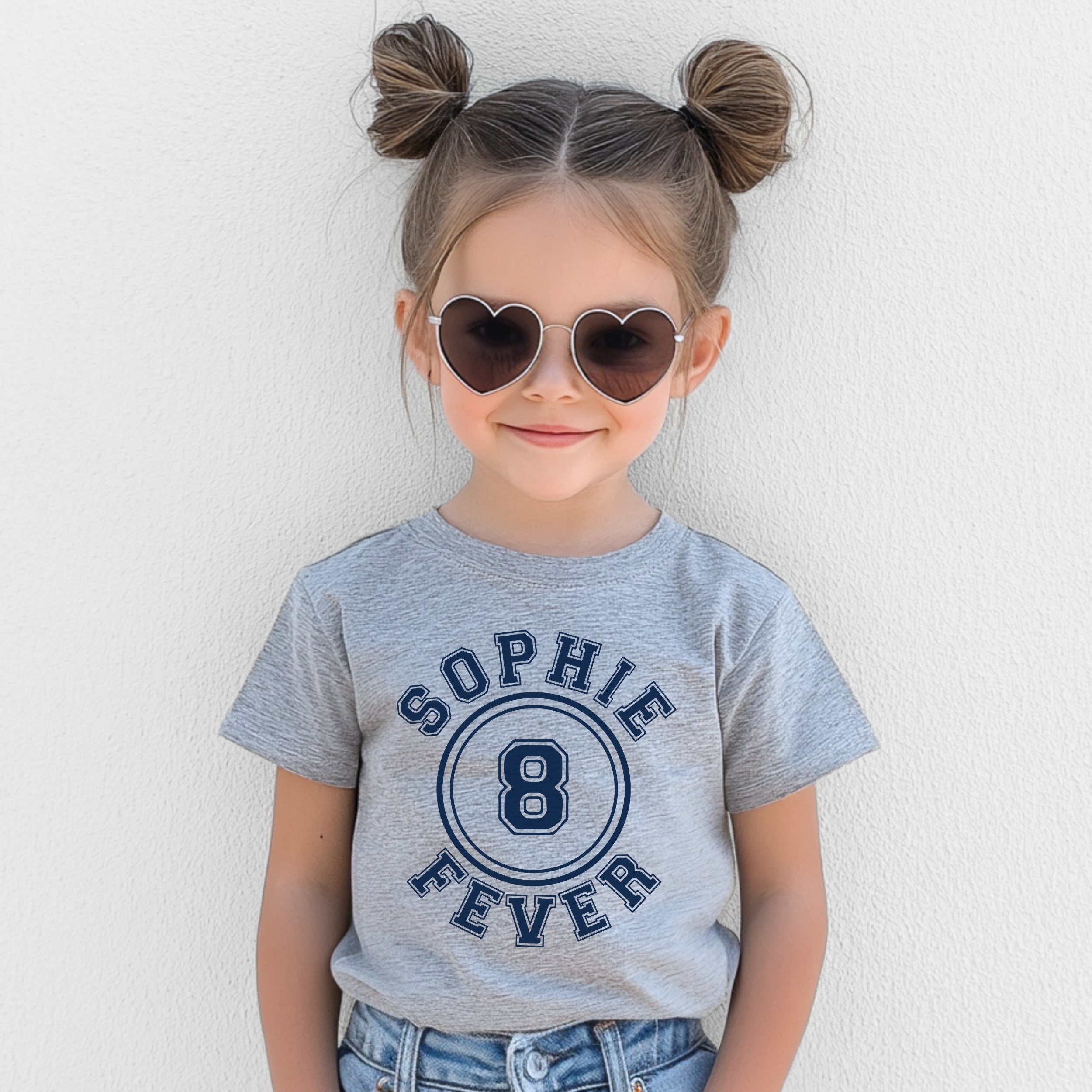 Child wearing a gray t-shirt with 'Sophie 8 Fever' design, heart-shaped sunglasses, and denim shorts against a light background.