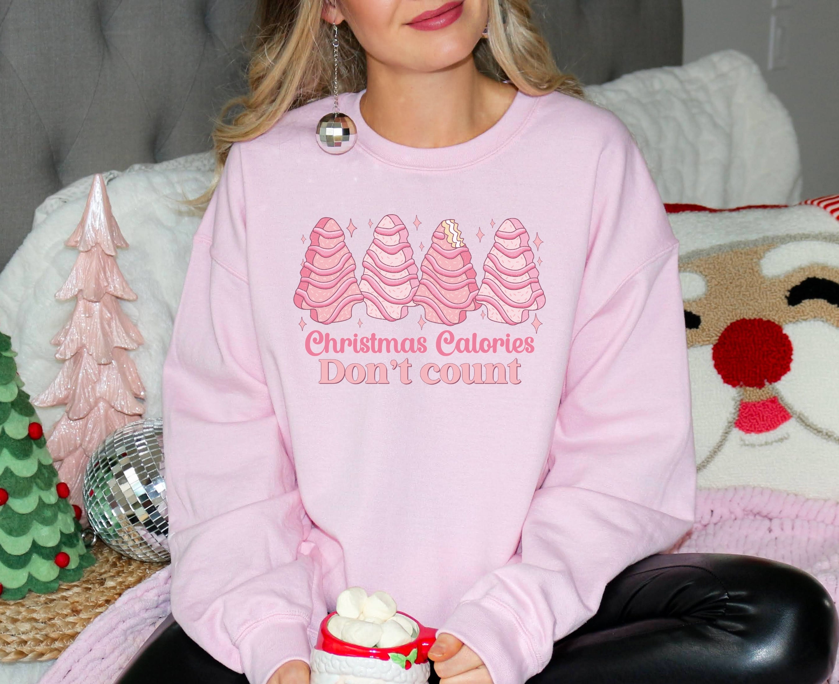 Girl wearing pink sweatshirt with pink Christmas tree cakes on it