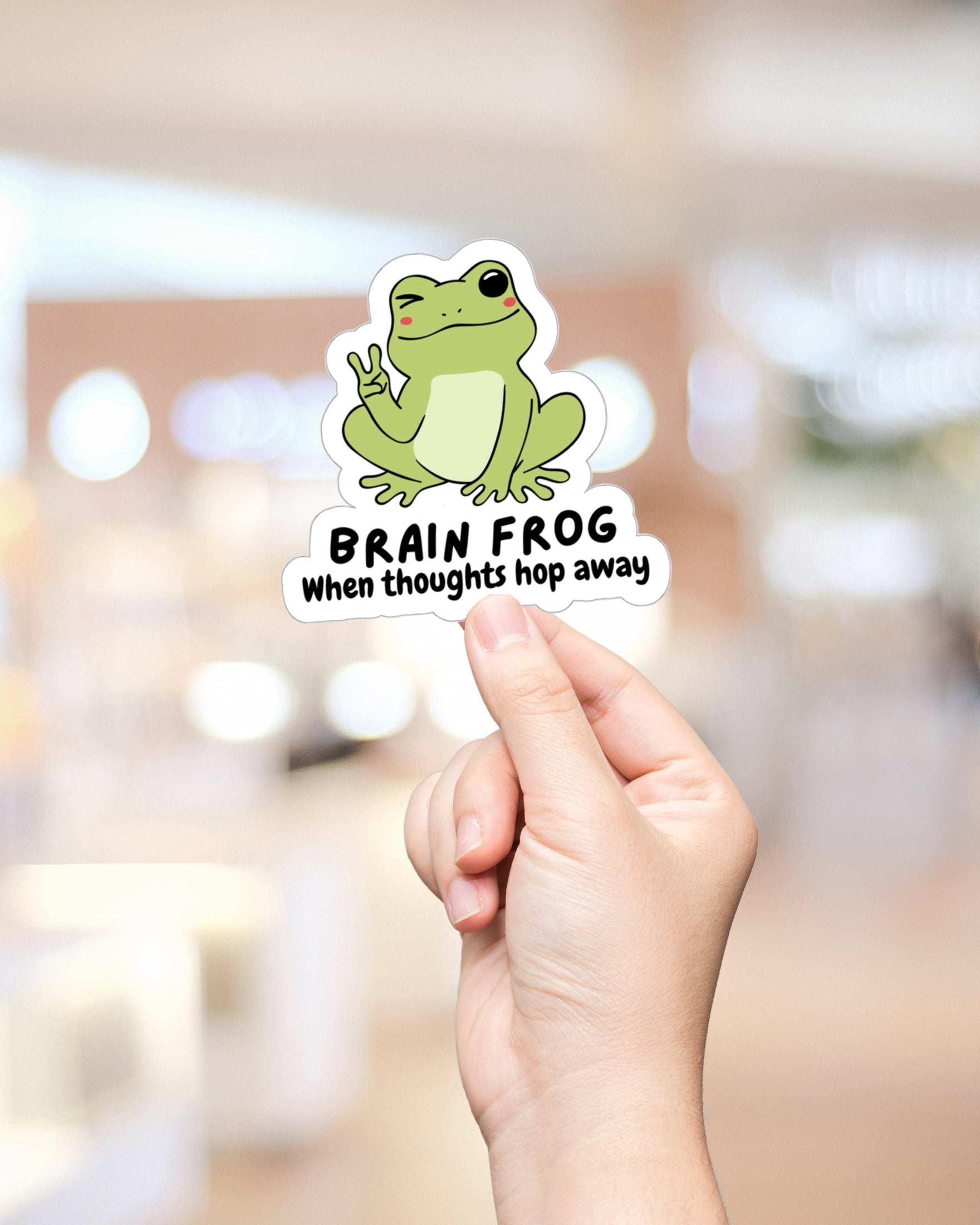 Sticker of a frog giving the peace sign being held up by hand