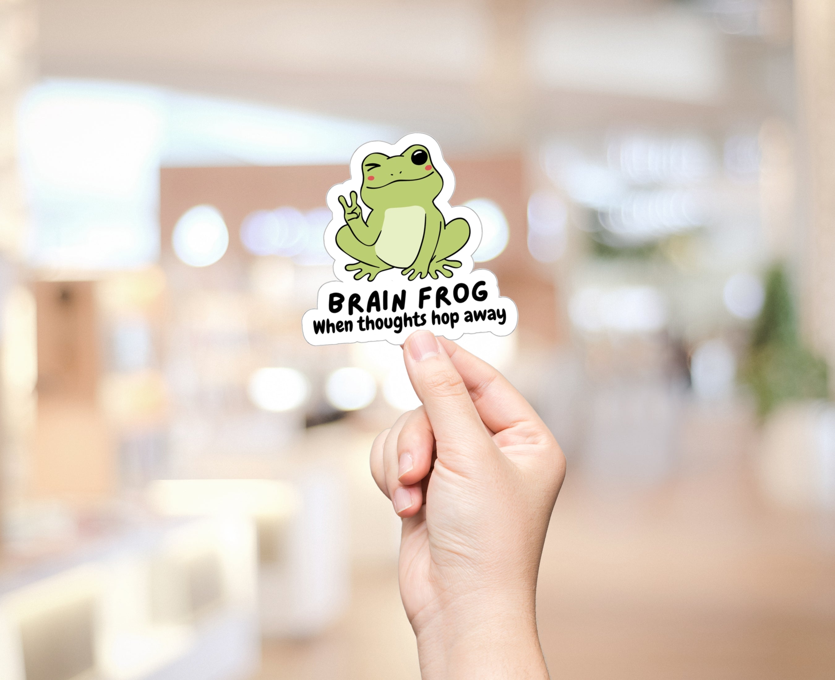 Sticker of a frog giving the peace sign being held up by hand