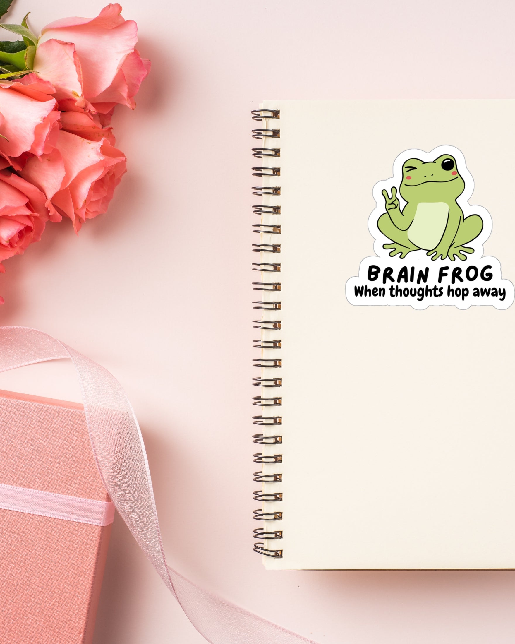 Sticker of a frog giving the peace sign on a notebook