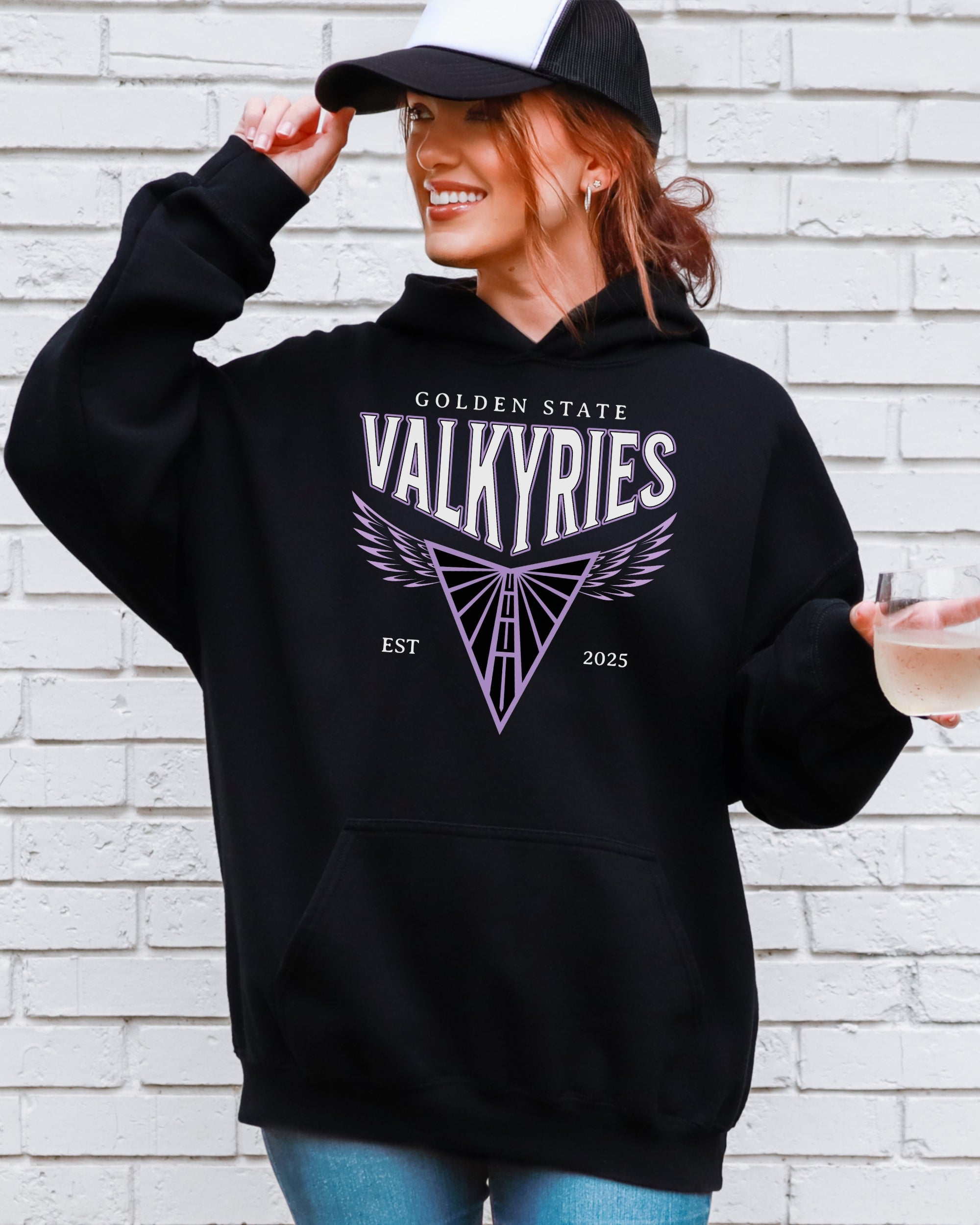 Person wearing a black hoodie with 'Golden State Valkyries' logo against a white brick wall.