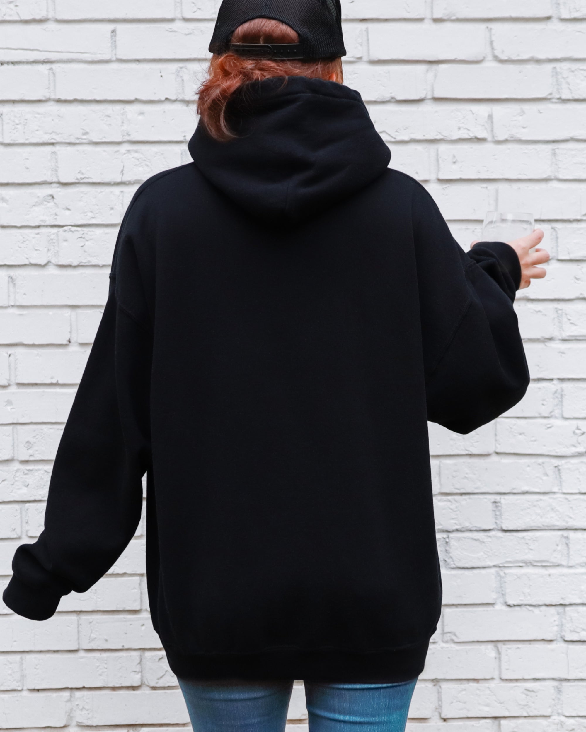 Person wearing a black hoodie and blue jeans against a white brick wall