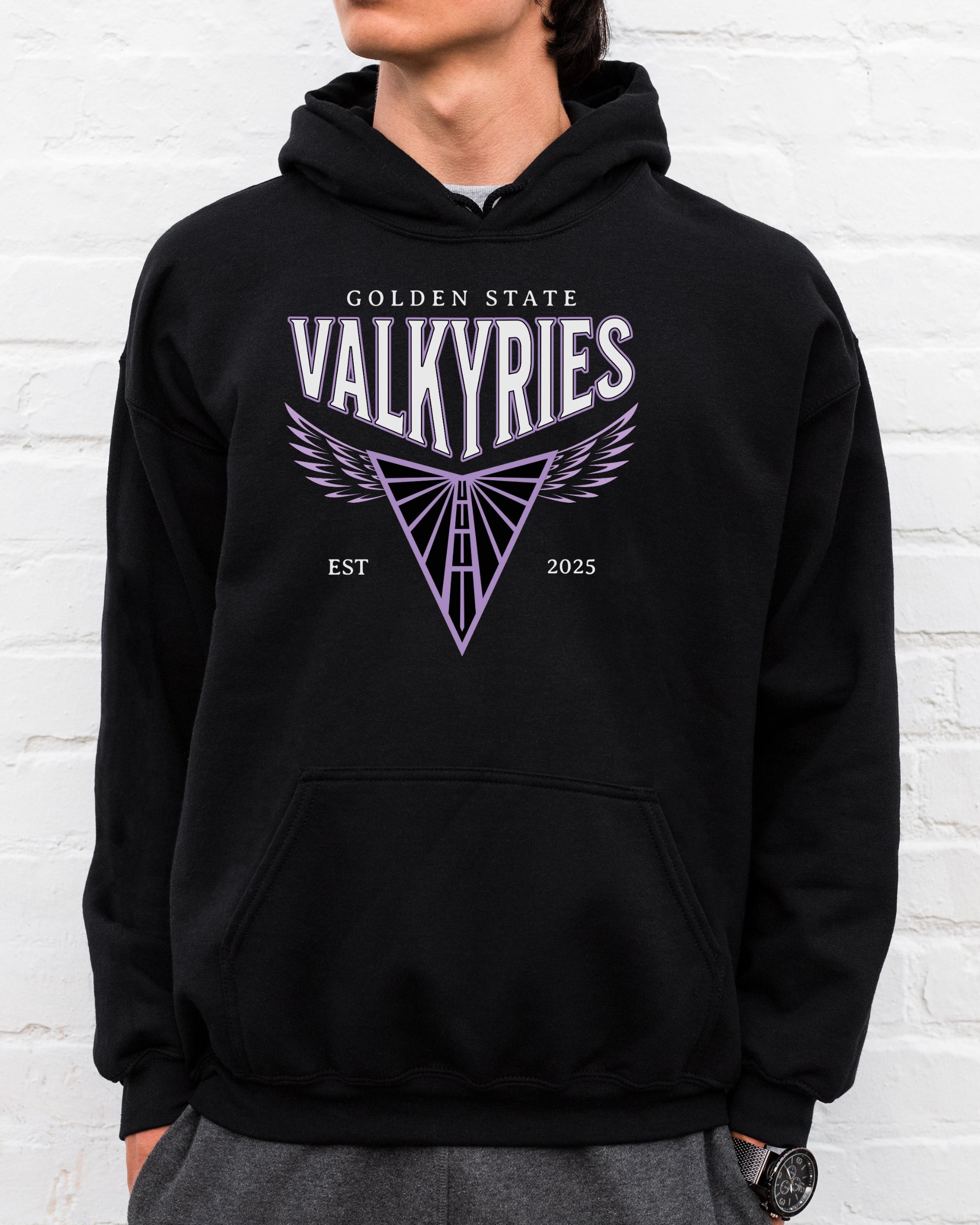 Person wearing a black hoodie with 'Golden State Valkyries' design against a white brick wall.