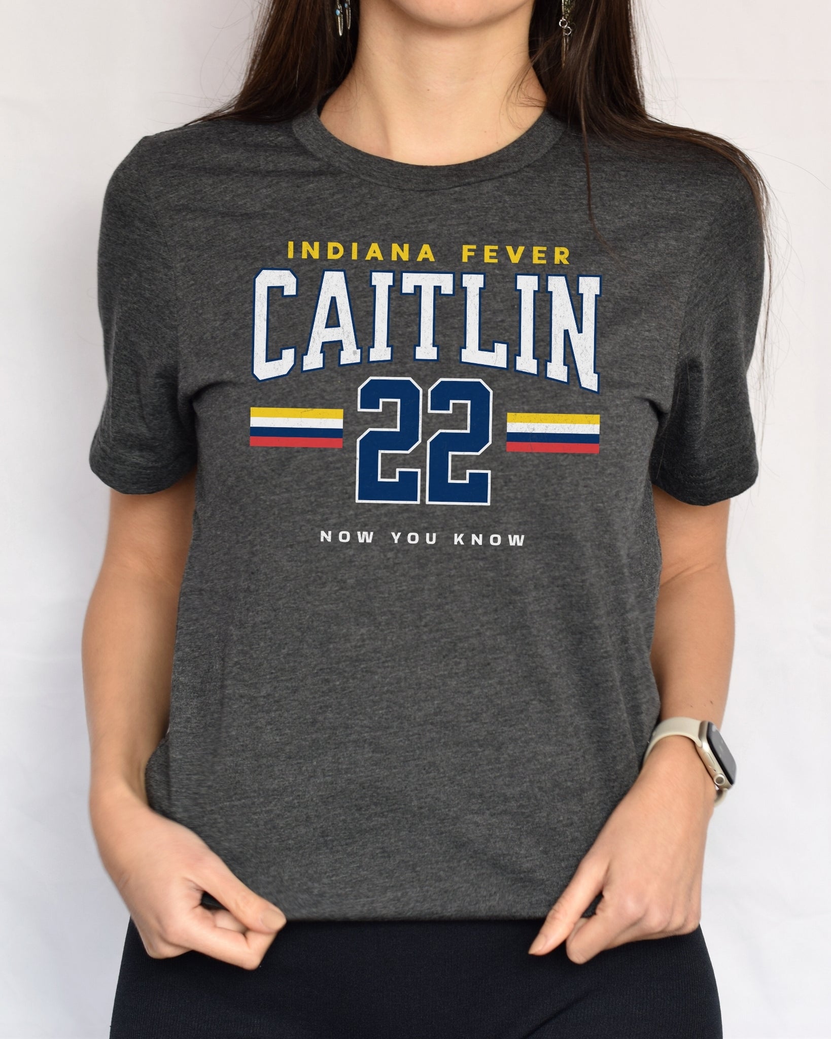 Person wearing a dark gray t-shirt with 'Indiana Fever Caitlin 22 Now You Know' text in front of white background