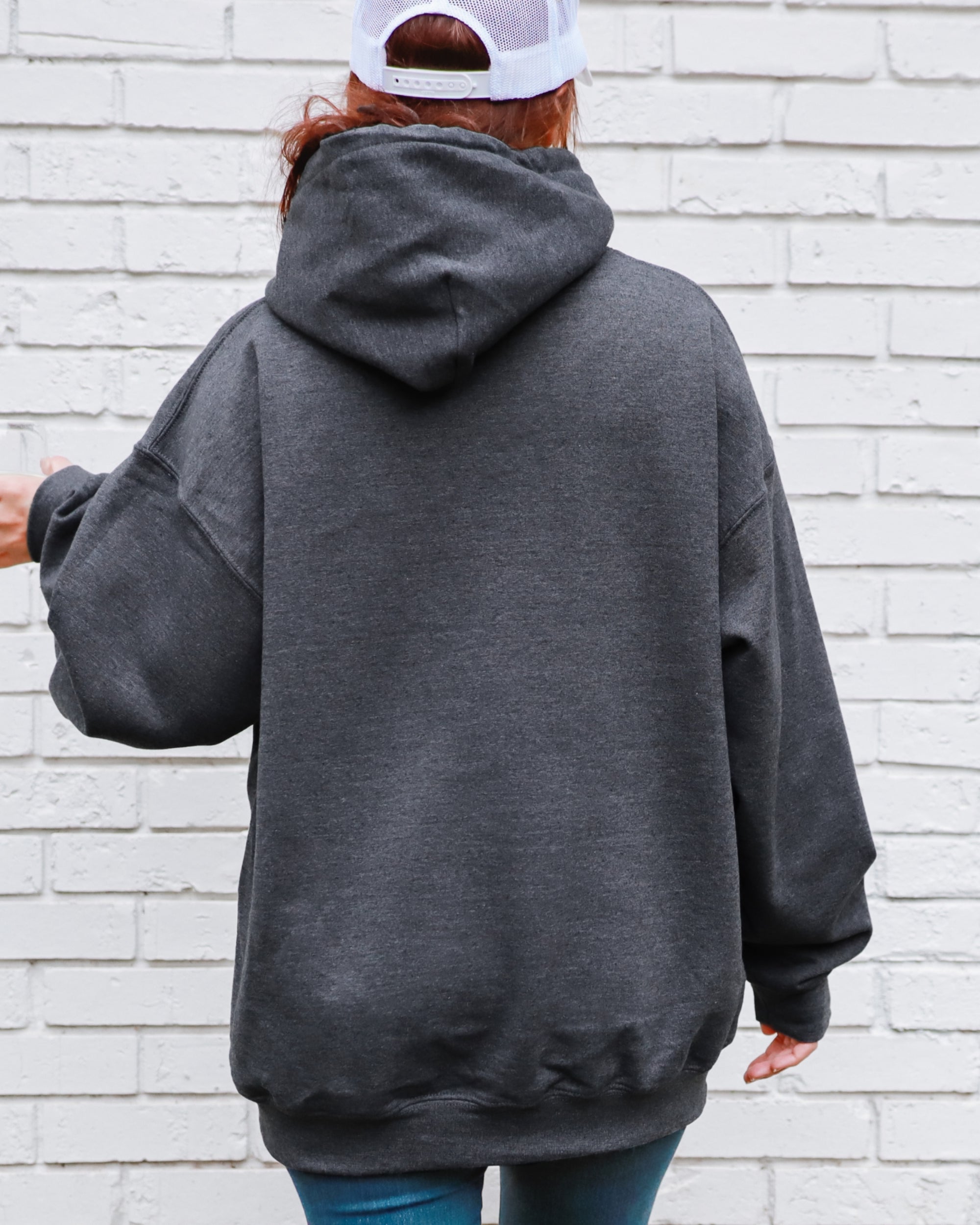 Person wearing a gray hoodie with a white brick wall background