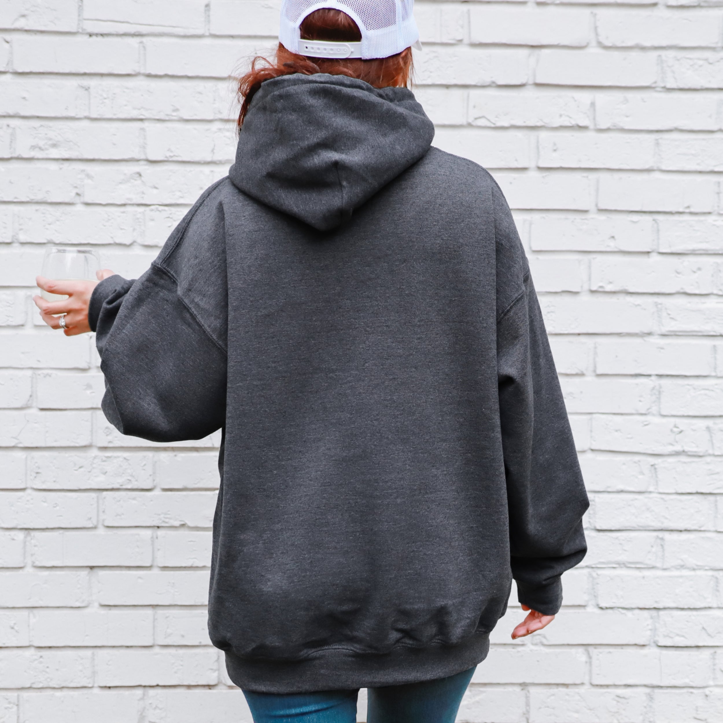Person wearing a gray hoodie with a white brick wall background