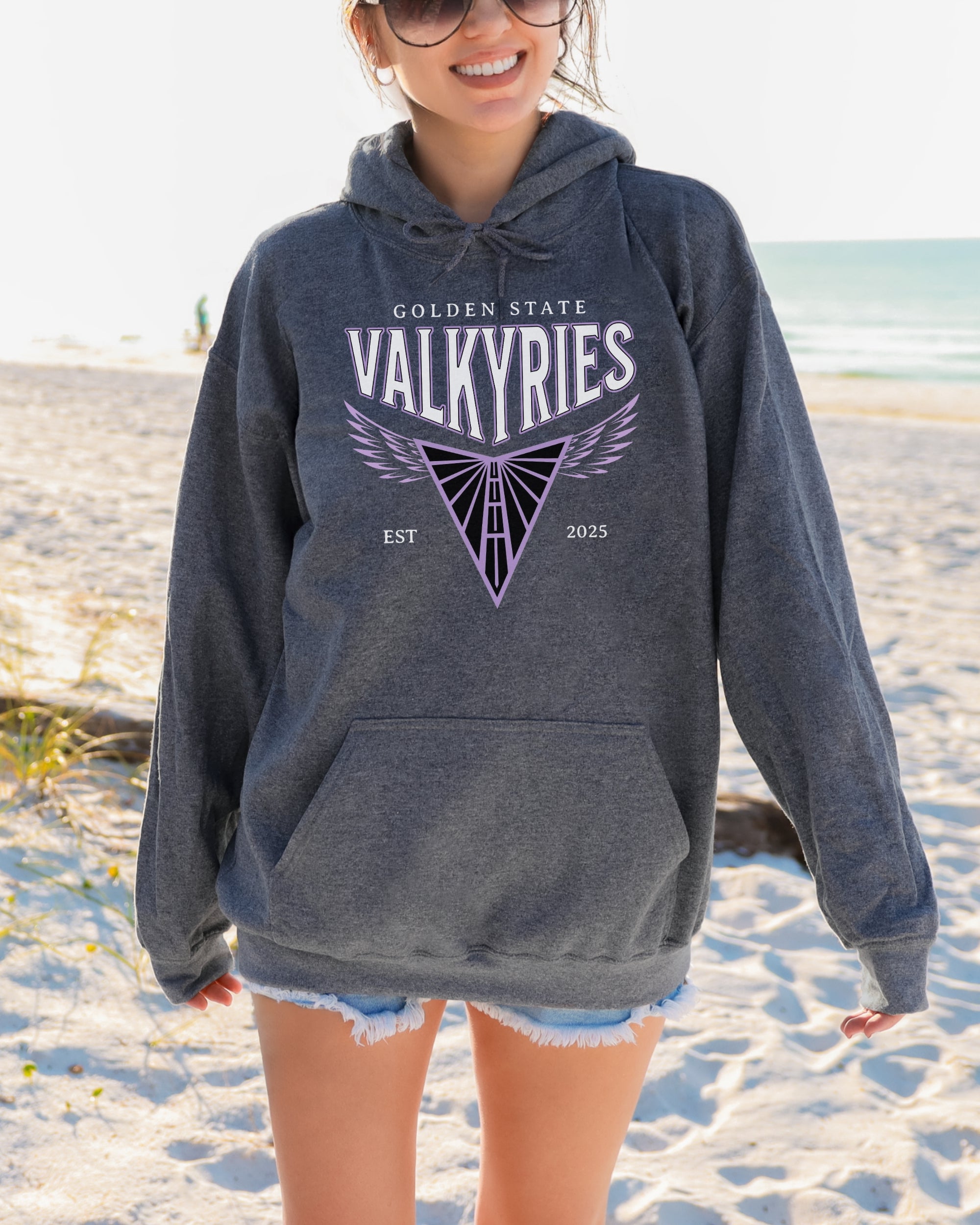 Person wearing a gray hoodie with 'Golden State Valkyries' on a beach