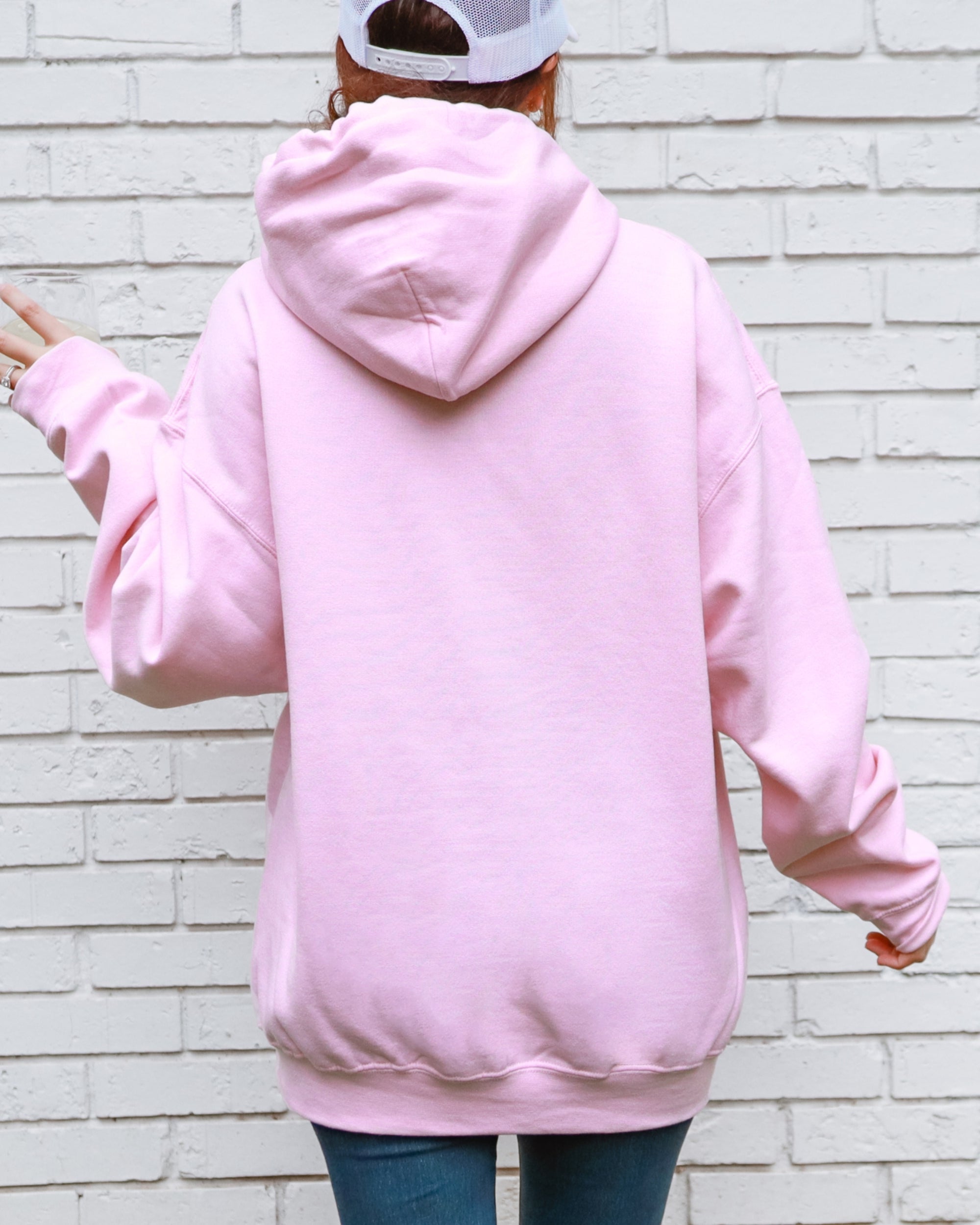 Person wearing a pink hoodie with a white brick wall background
