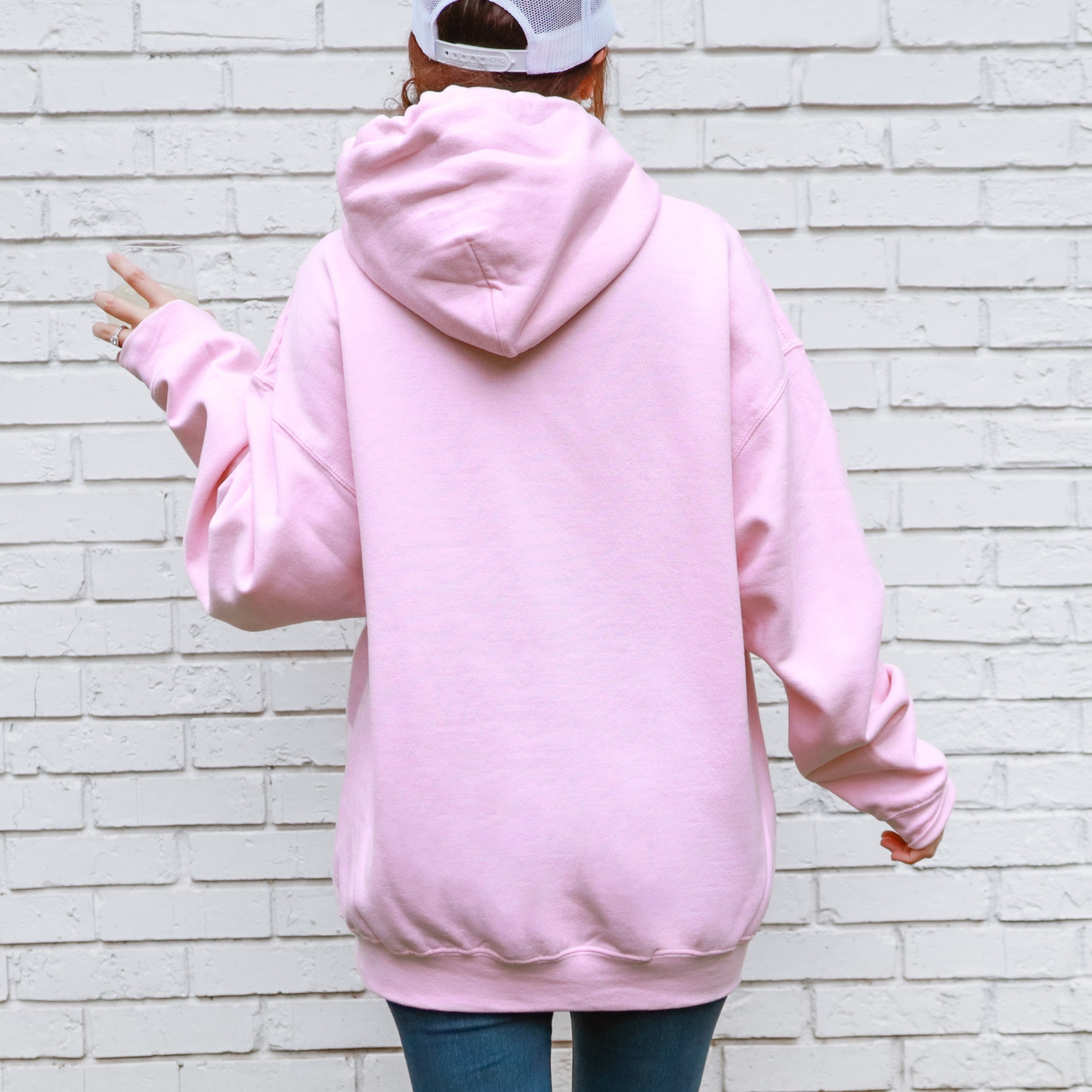 Person wearing a pink hoodie with a white brick wall background