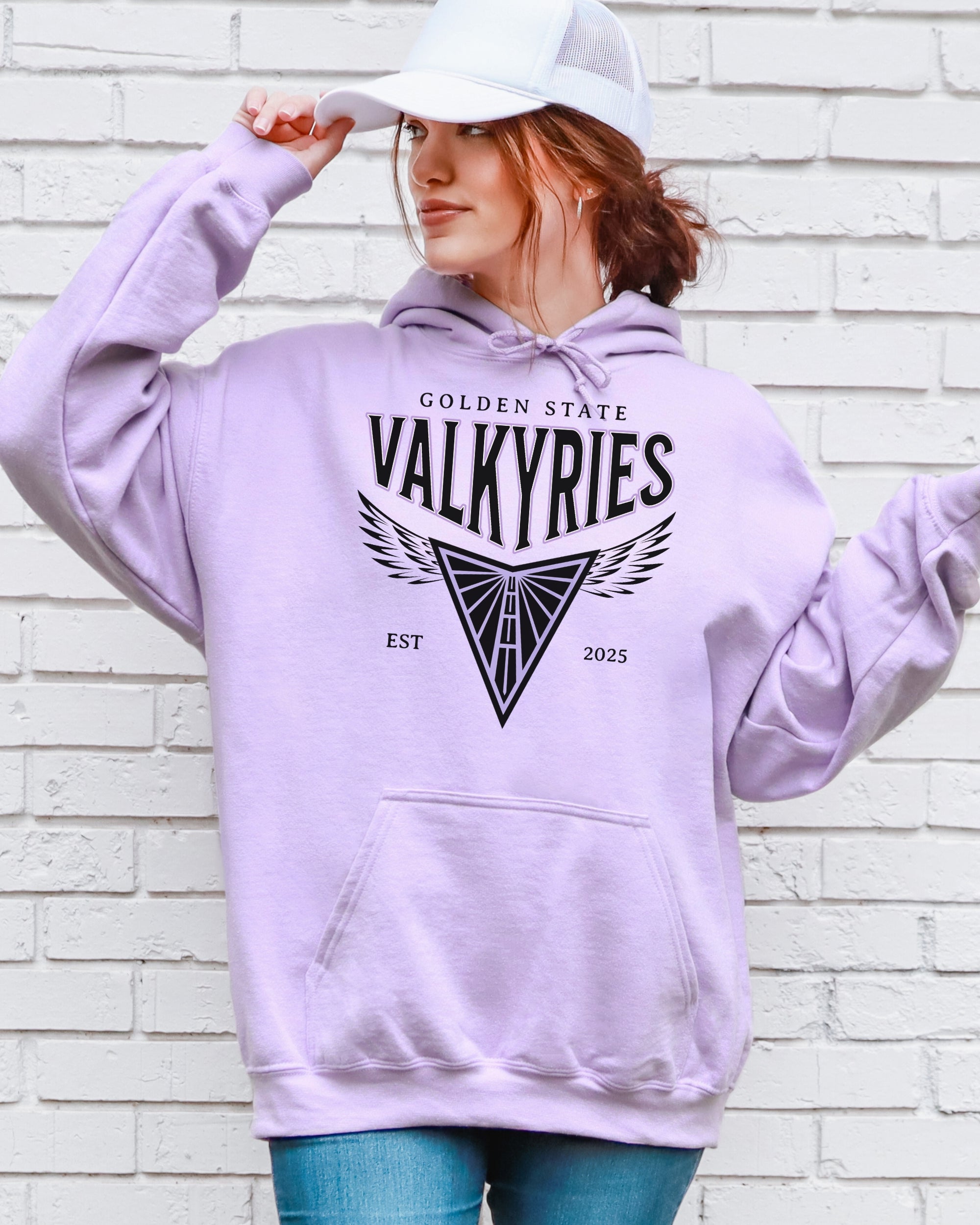 Person wearing a lavender hoodie with 'Golden State Valkyries' text and design, standing against a white brick wall.
