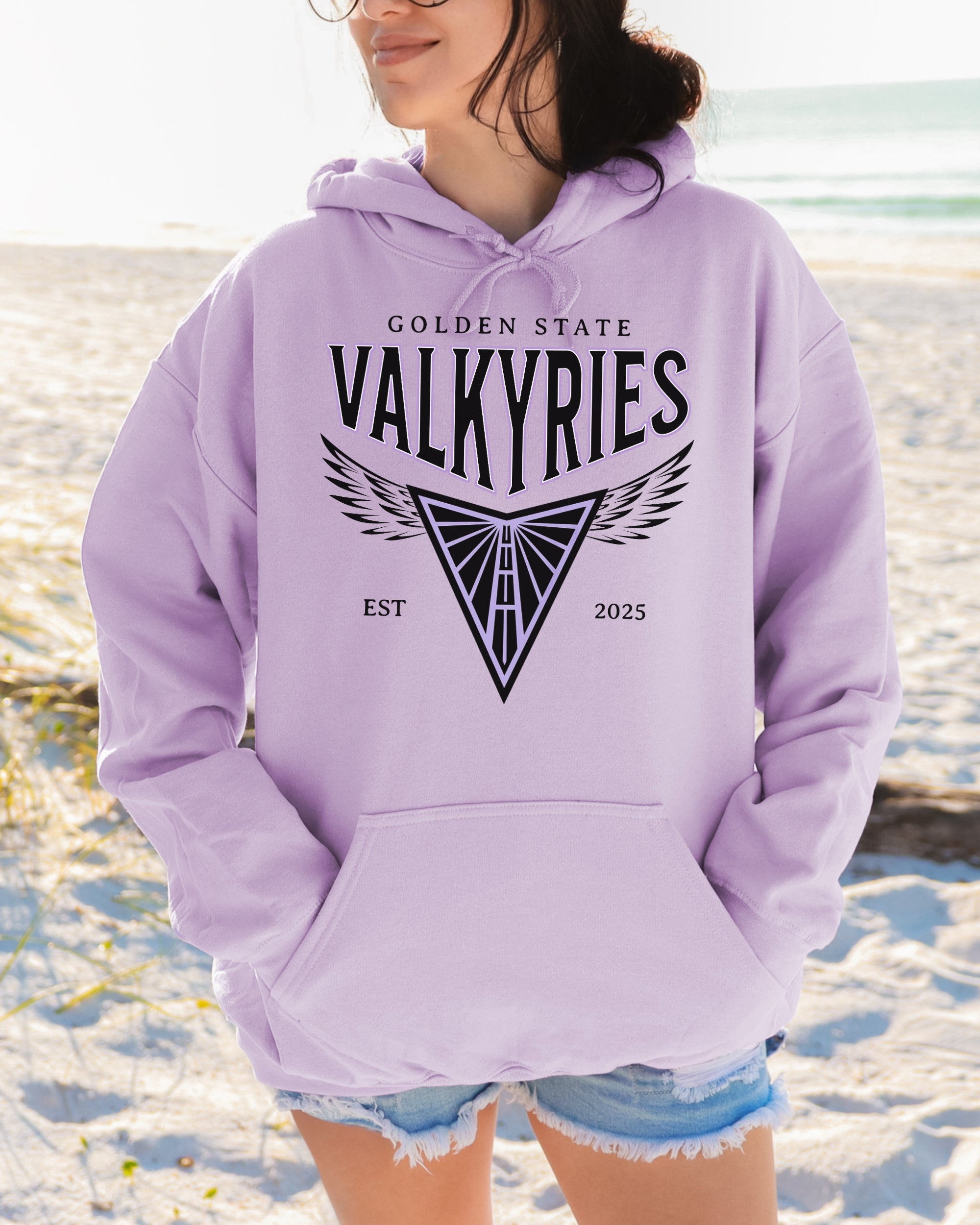 Person wearing a lavender hoodie with 'Golden State Valkyries' text and design on a beach.