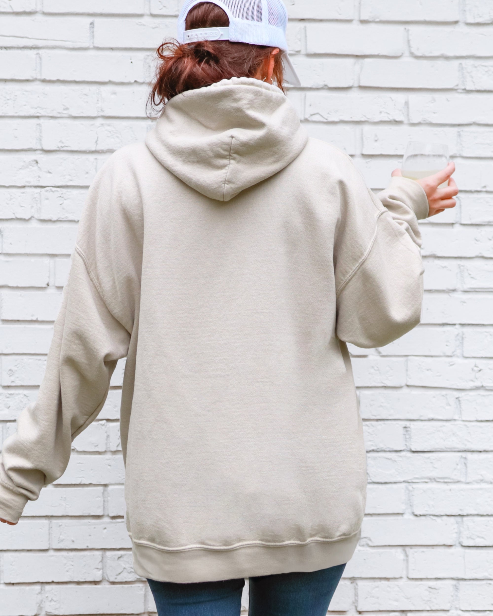 Person wearing a beige hoodie with a white brick wall background