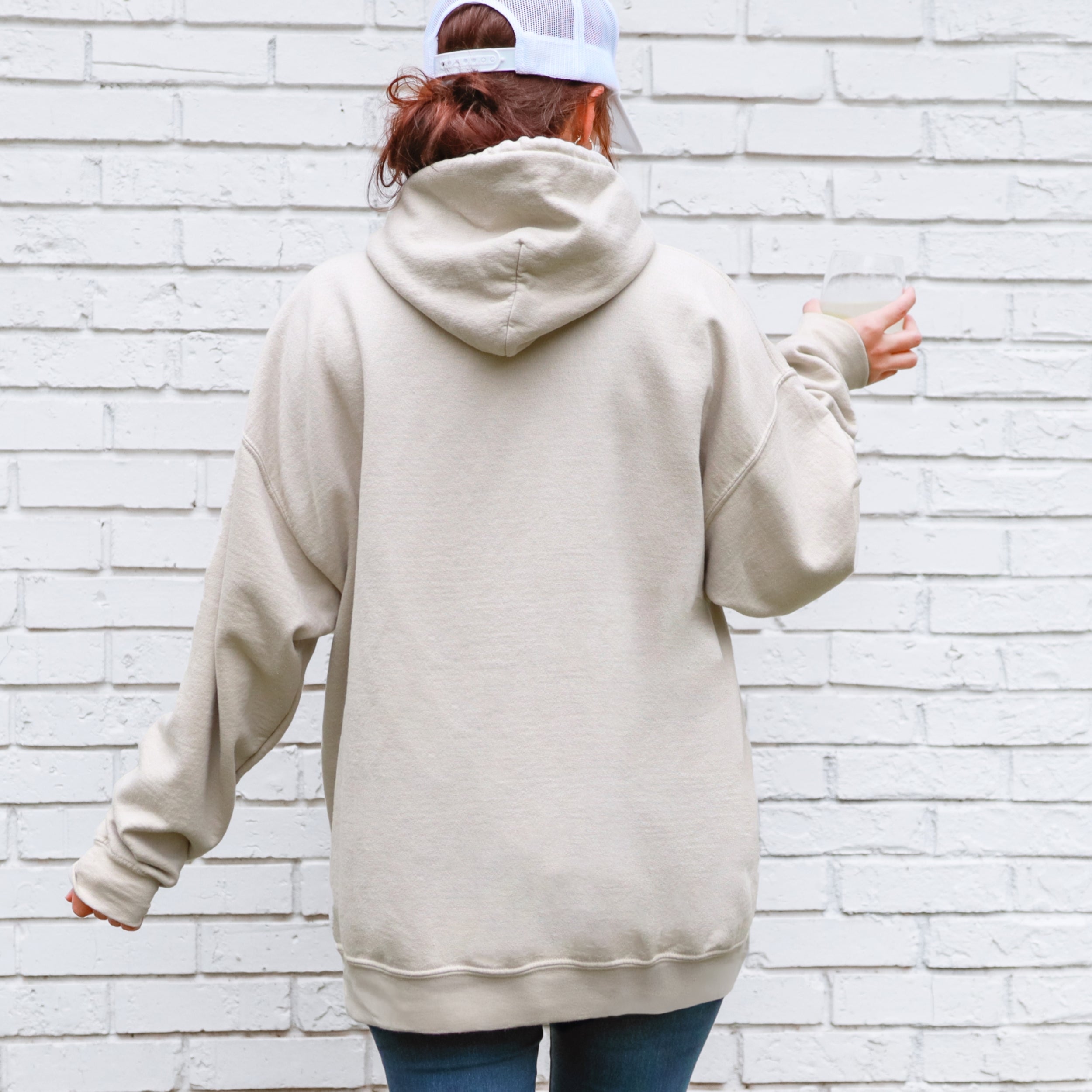 Person wearing a beige hoodie with a white brick wall background