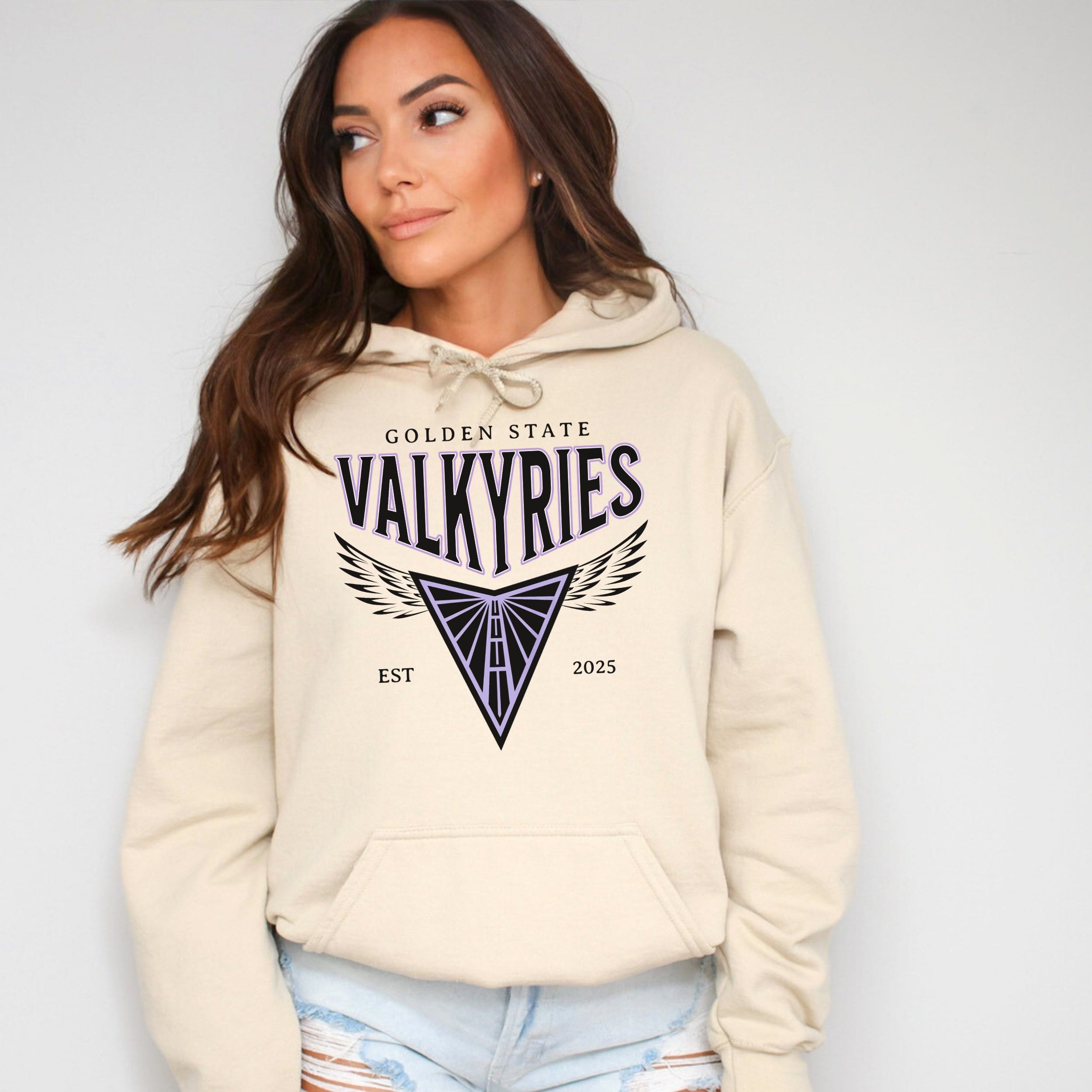 Woman wearing a beige hoodie with 'Golden State Valkyries' design on a plain background