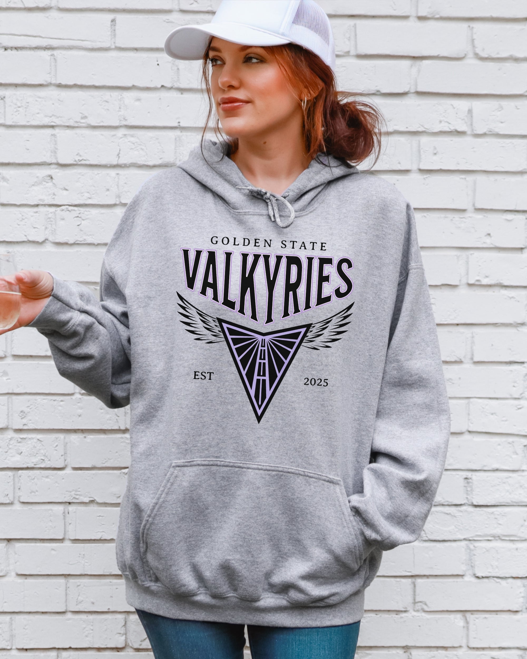 Person wearing a gray hoodie with 'Golden State Valkyries' text and logo against a white brick wall.