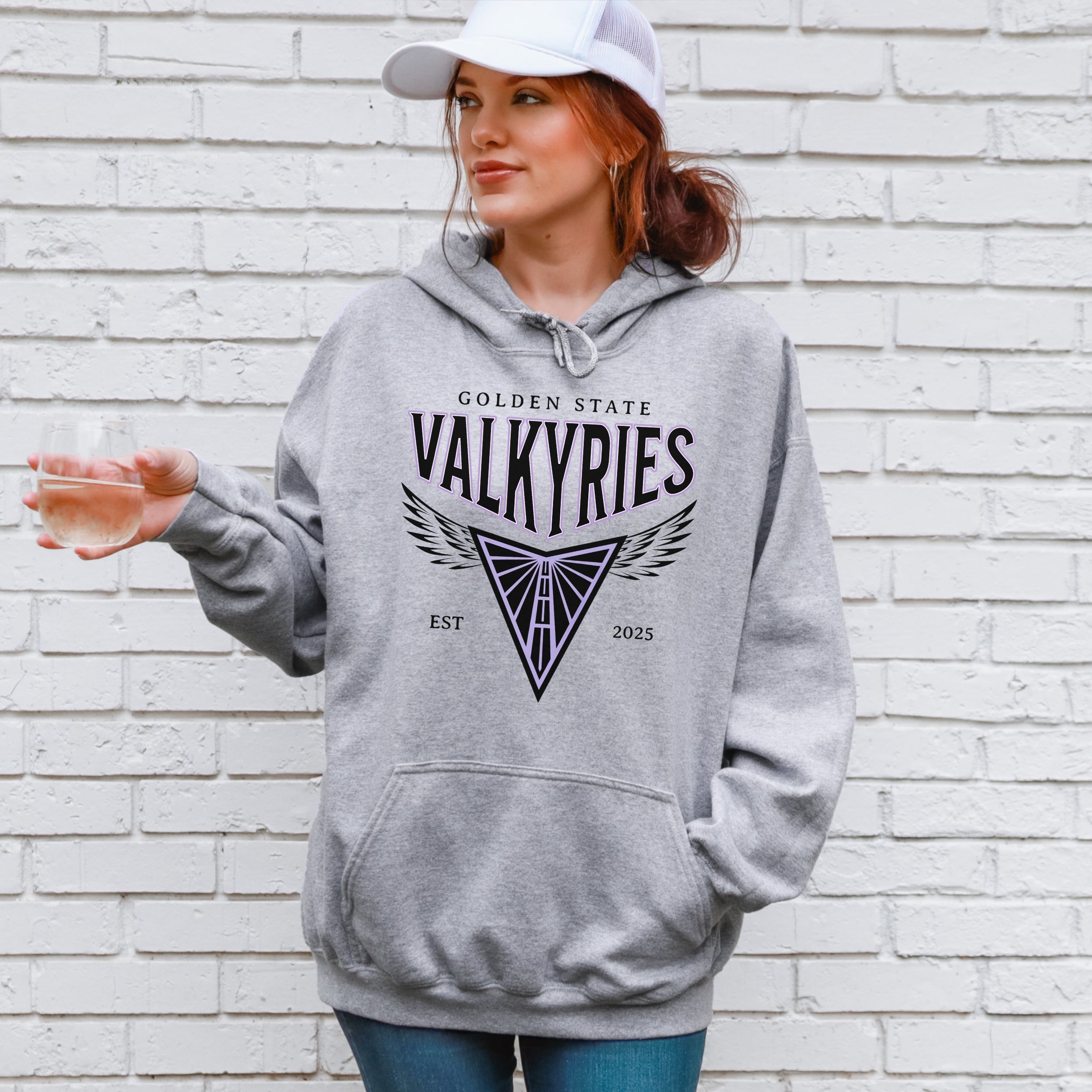 Person wearing a gray hoodie with 'Golden State Valkyries' text and logo against a white brick wall.