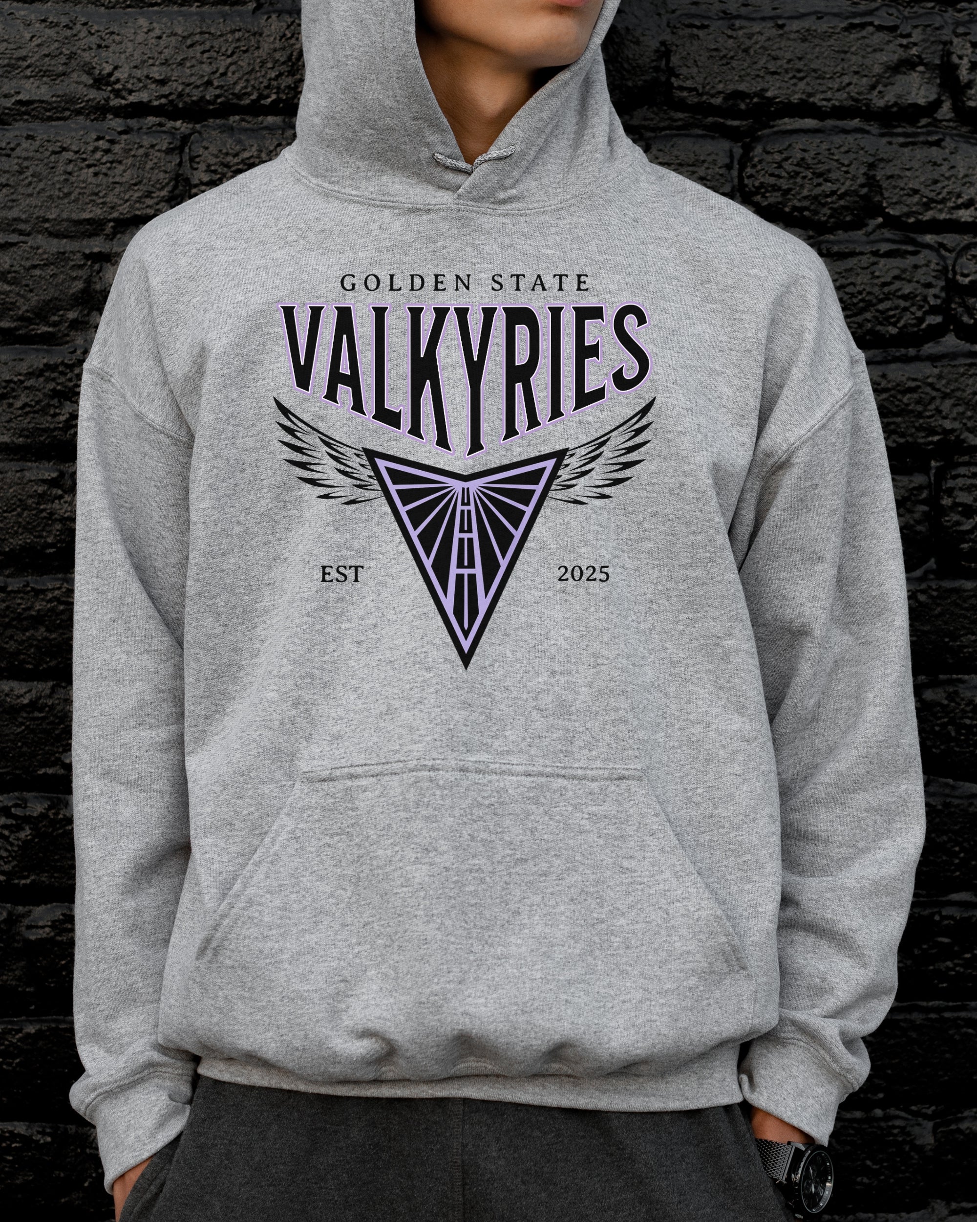 Person wearing a gray hoodie with 'Golden State Valkyries' design against a dark brick wall.
