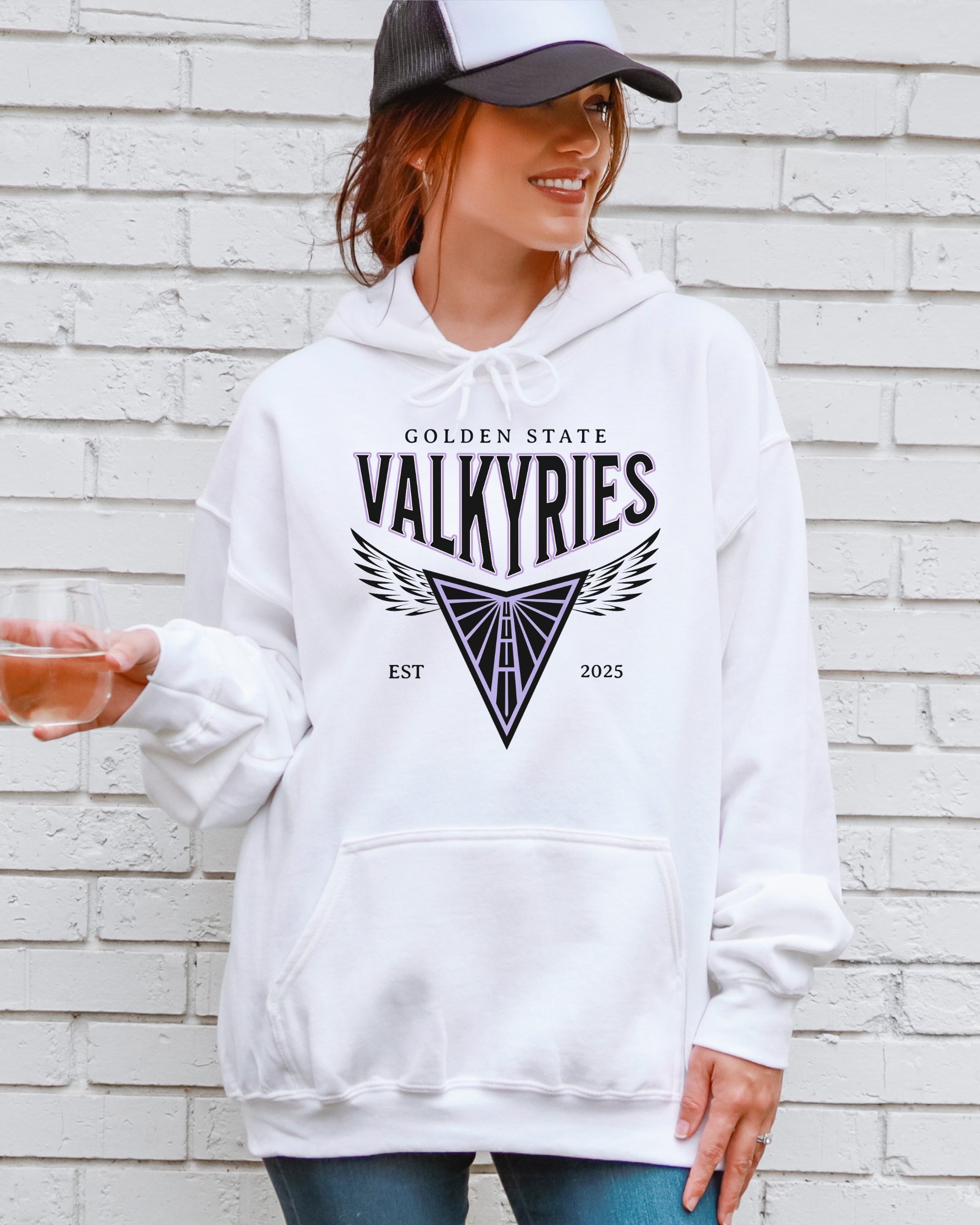 Person wearing a white hoodie with 'Golden State Valkyries' logo against a brick wall.