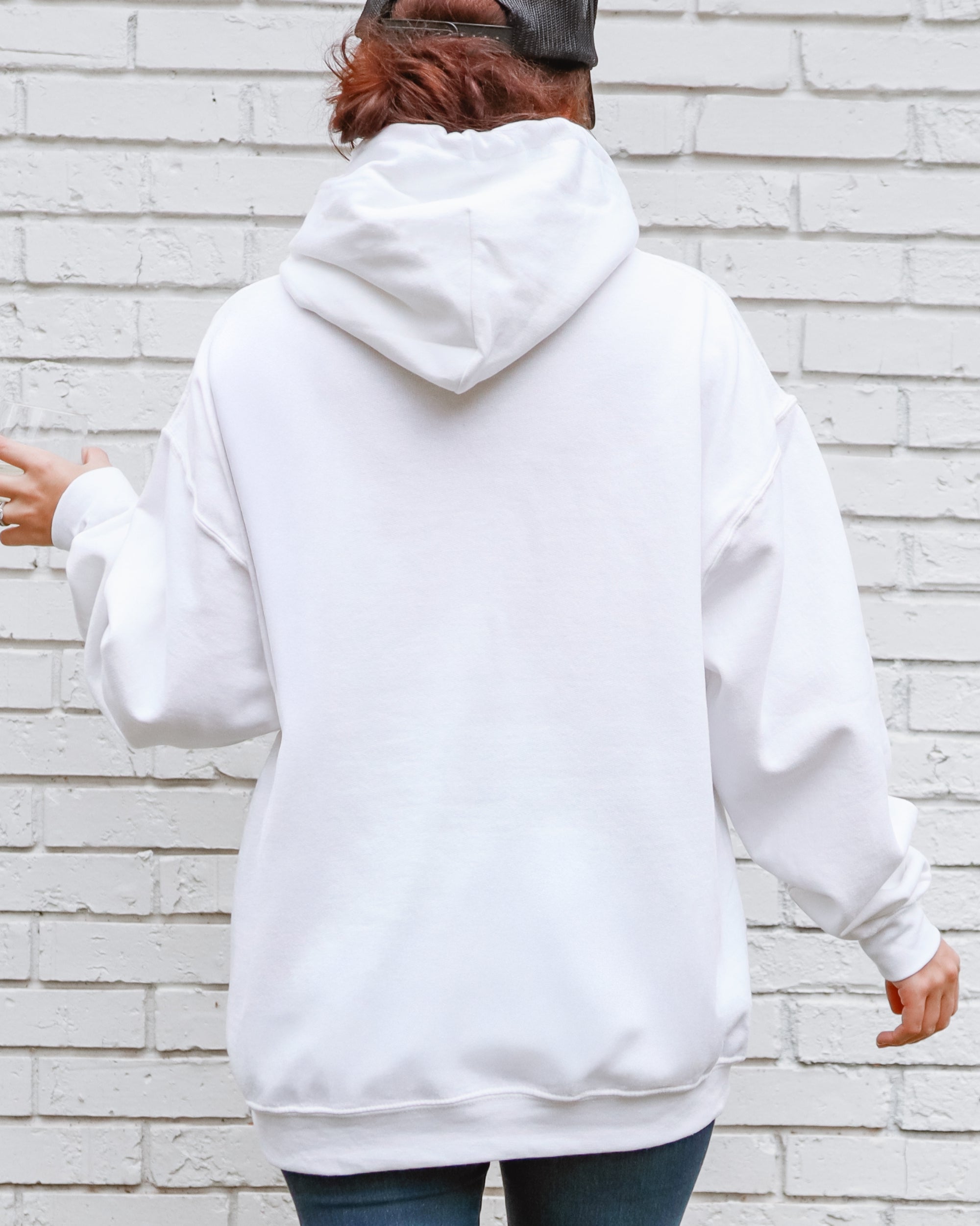 Person wearing a white hoodie standing against a light brick wall.