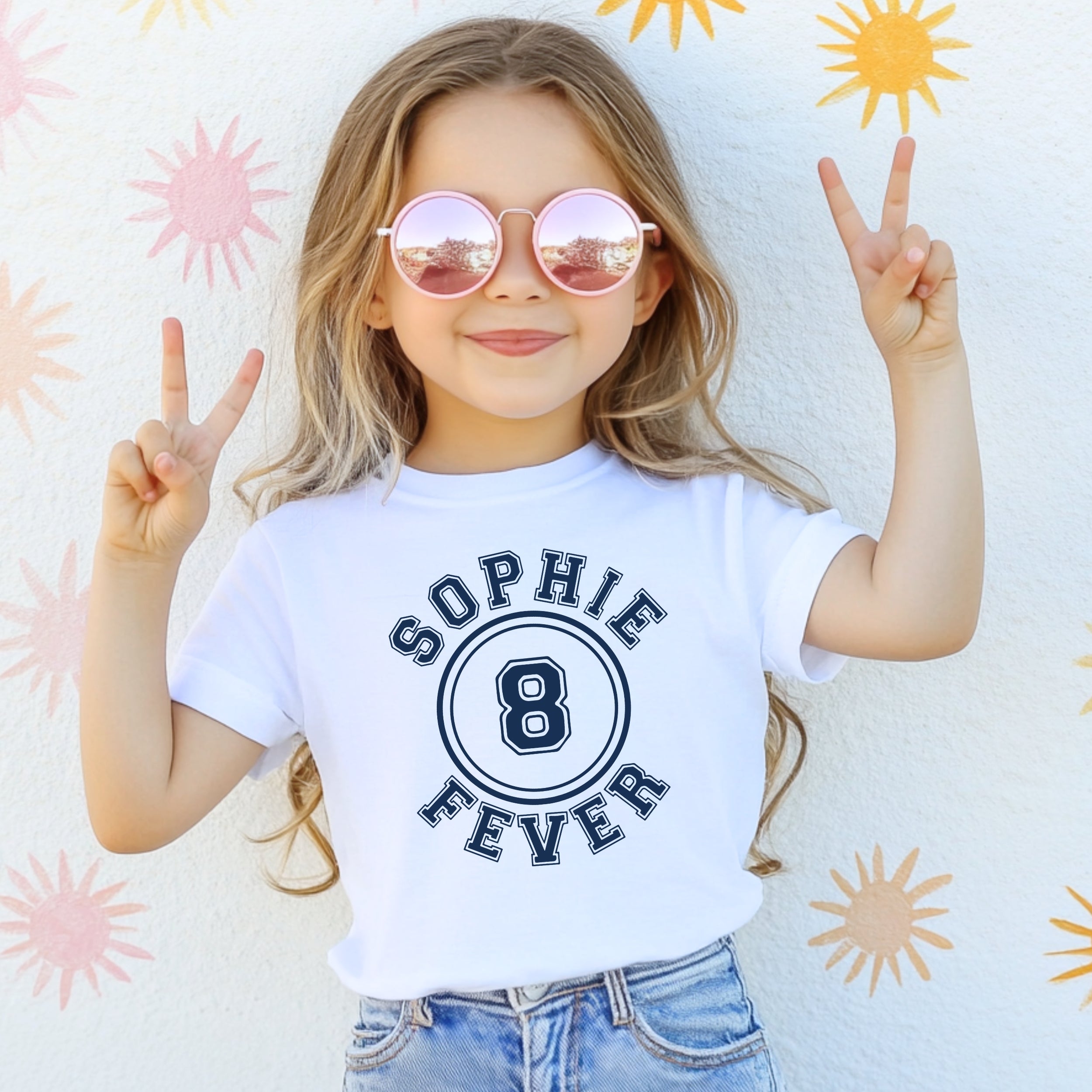 Child wearing a white t-shirt with 'Sophie 8 Fever' design, making peace signs against a sun-patterned background.