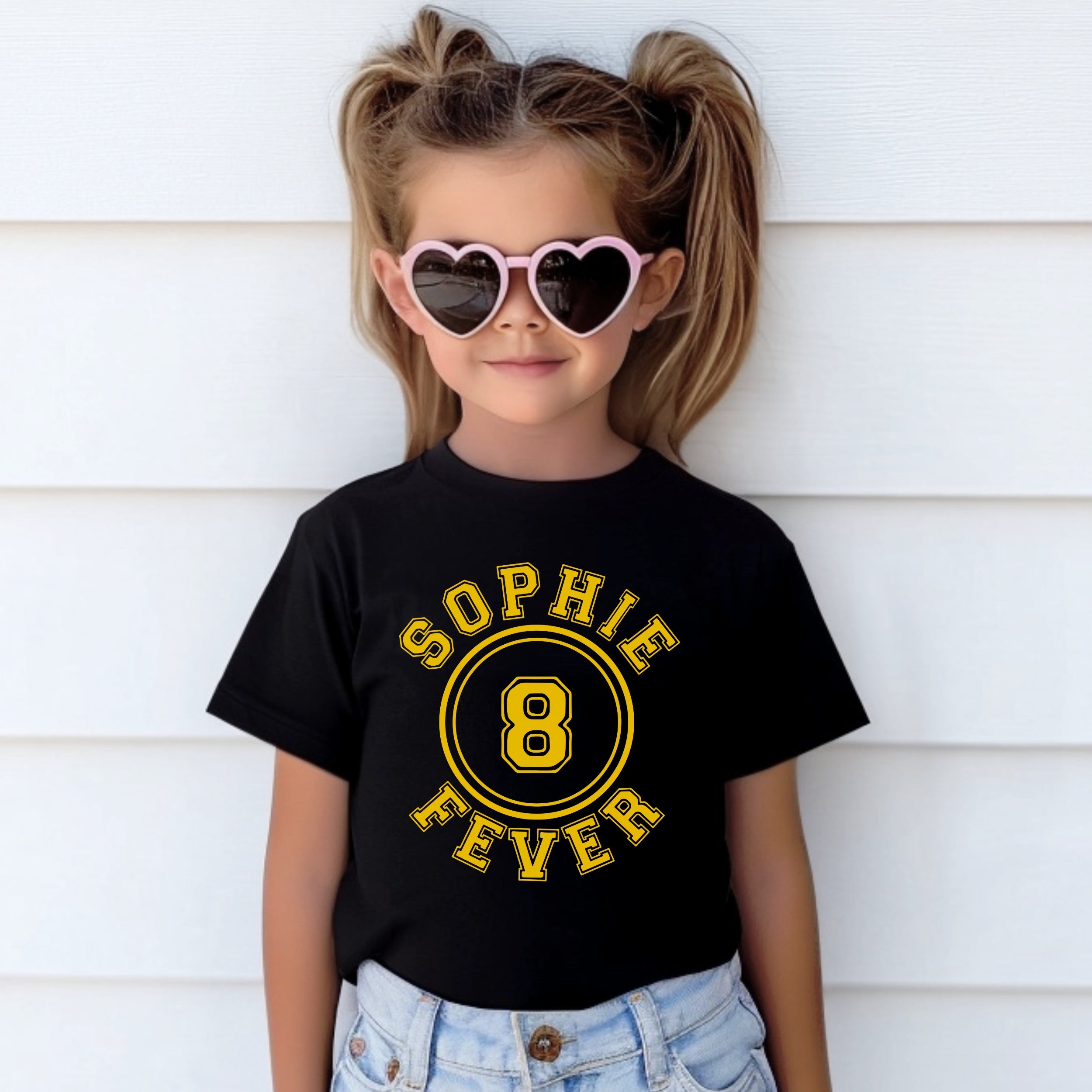 Child wearing a black t-shirt with 'Sophie 8 Fever' design, heart-shaped sunglasses, and denim shorts against a white background.