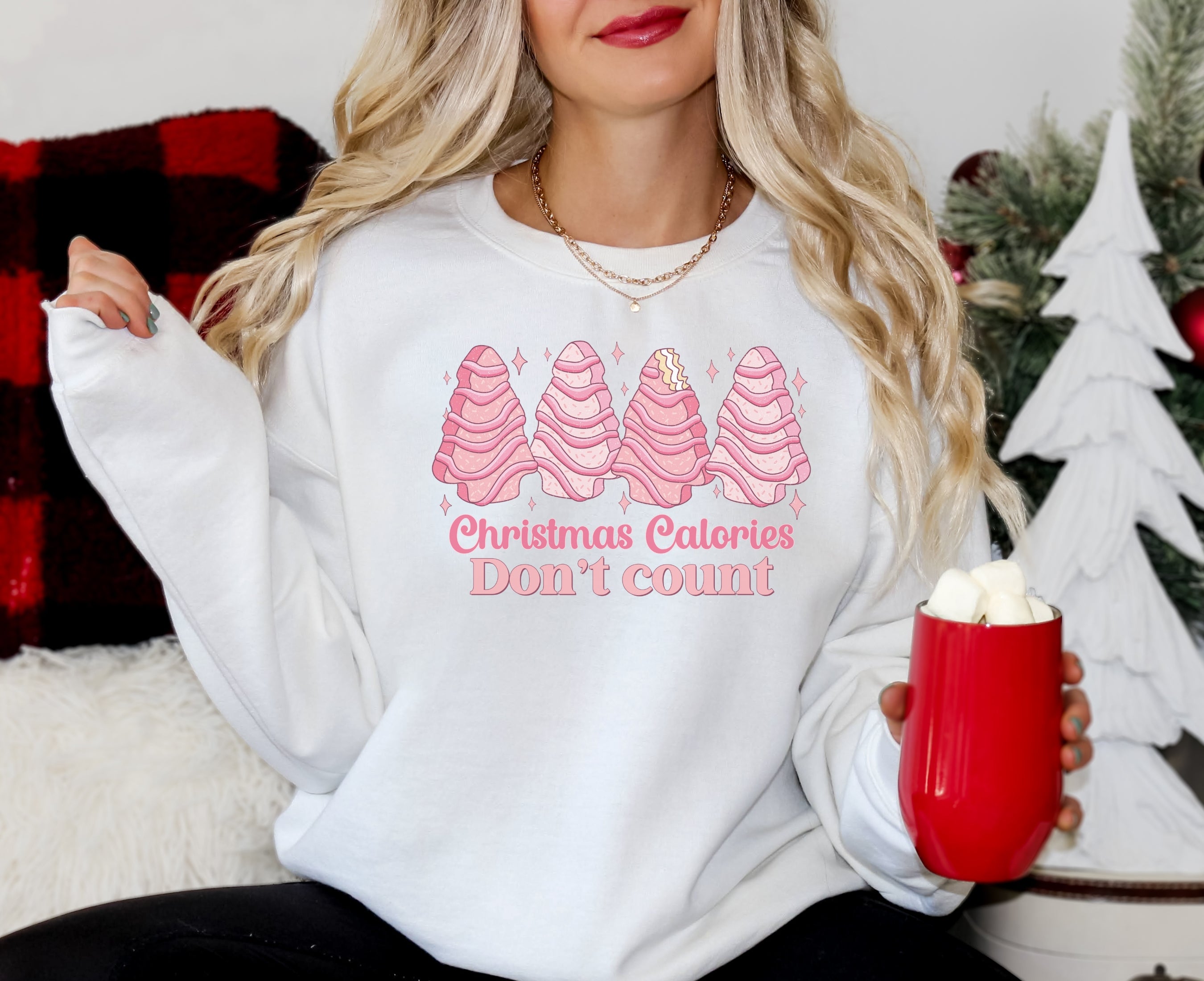 Girl wearing white sweatshirt with pink Christmas tree cakes on it