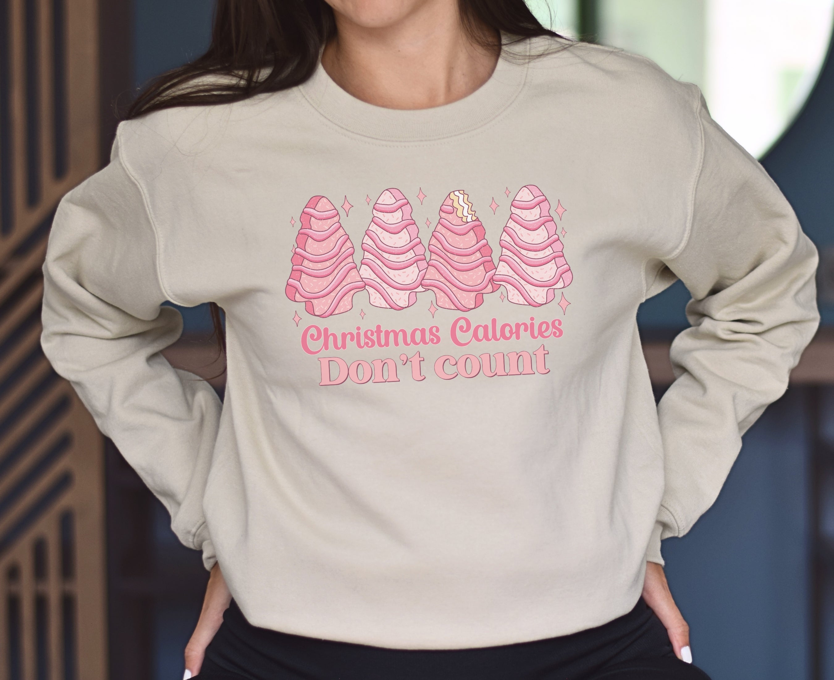 Girl wearing sand sweatshirt with pink Christmas tree cakes on it