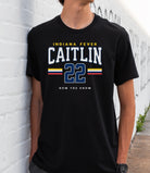 Person wearing a black t-shirt with 'Indiana Fever Caitlin 22 Now You Know' text against a white brick wall.