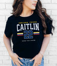 Person wearing a black t-shirt with 'Indiana Fever Caitlin 22 Now You Know' text against a white brick wall.