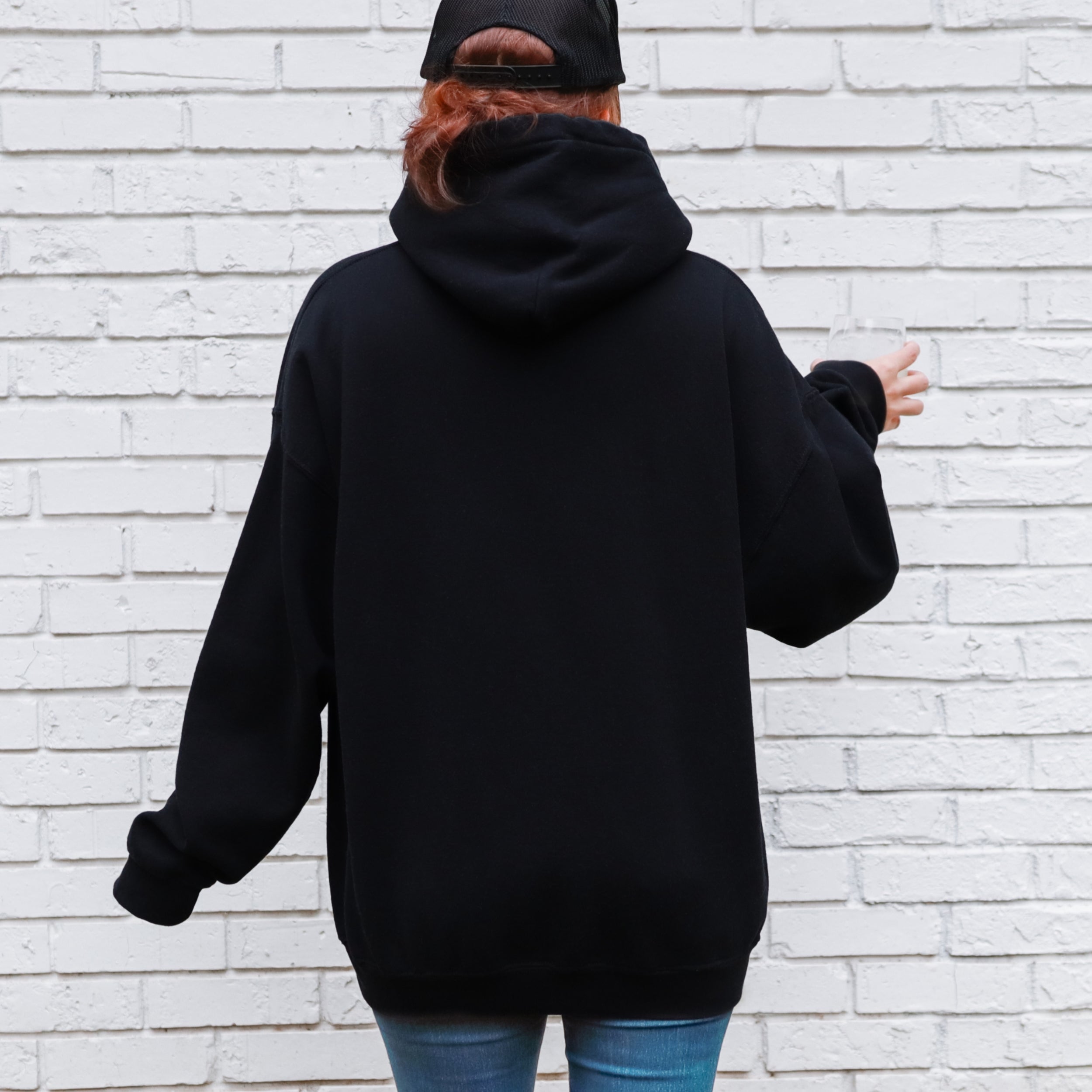 Person wearing a black hoodie and blue jeans against a white brick wall