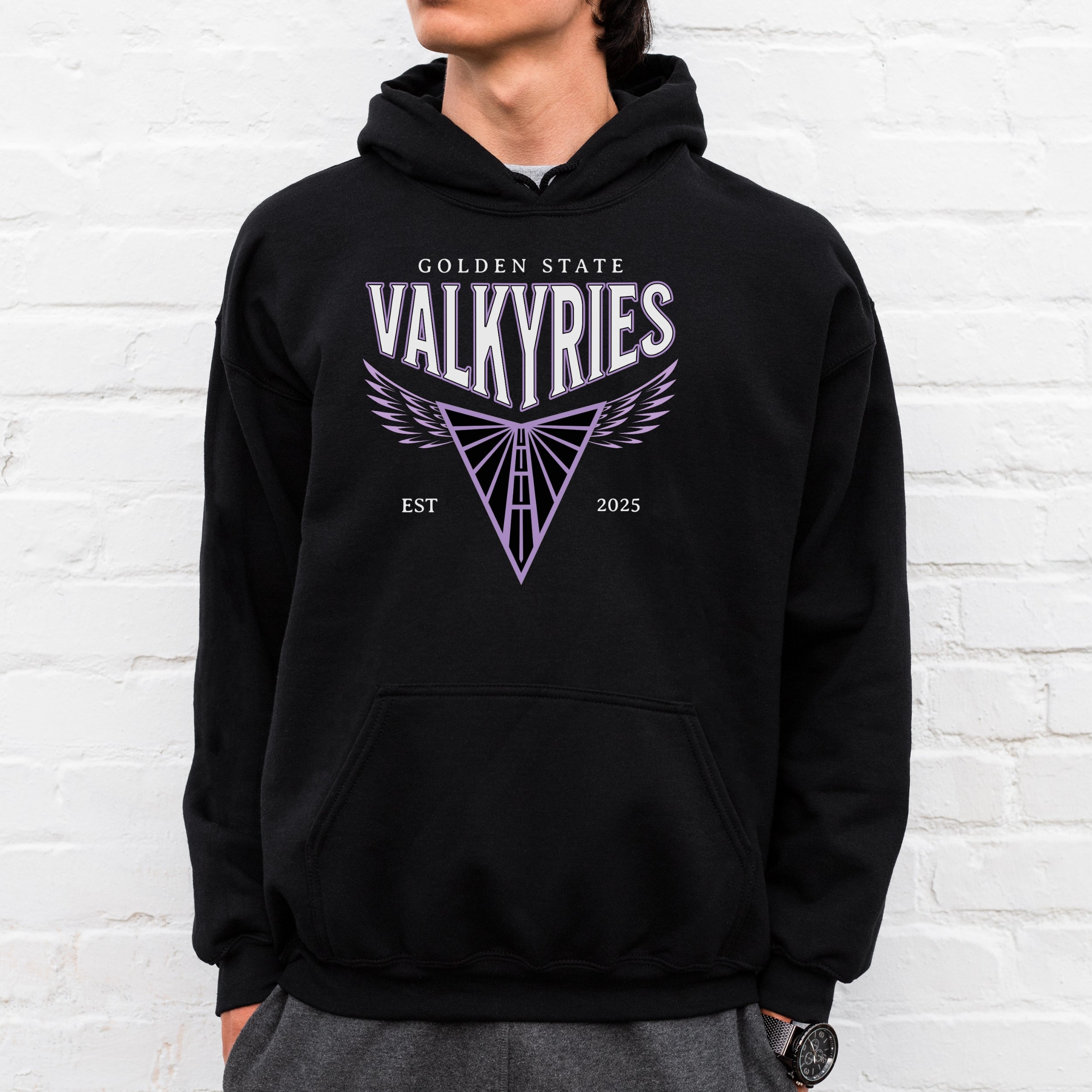 Person wearing a black hoodie with 'Golden State Valkyries' design against a white brick wall.