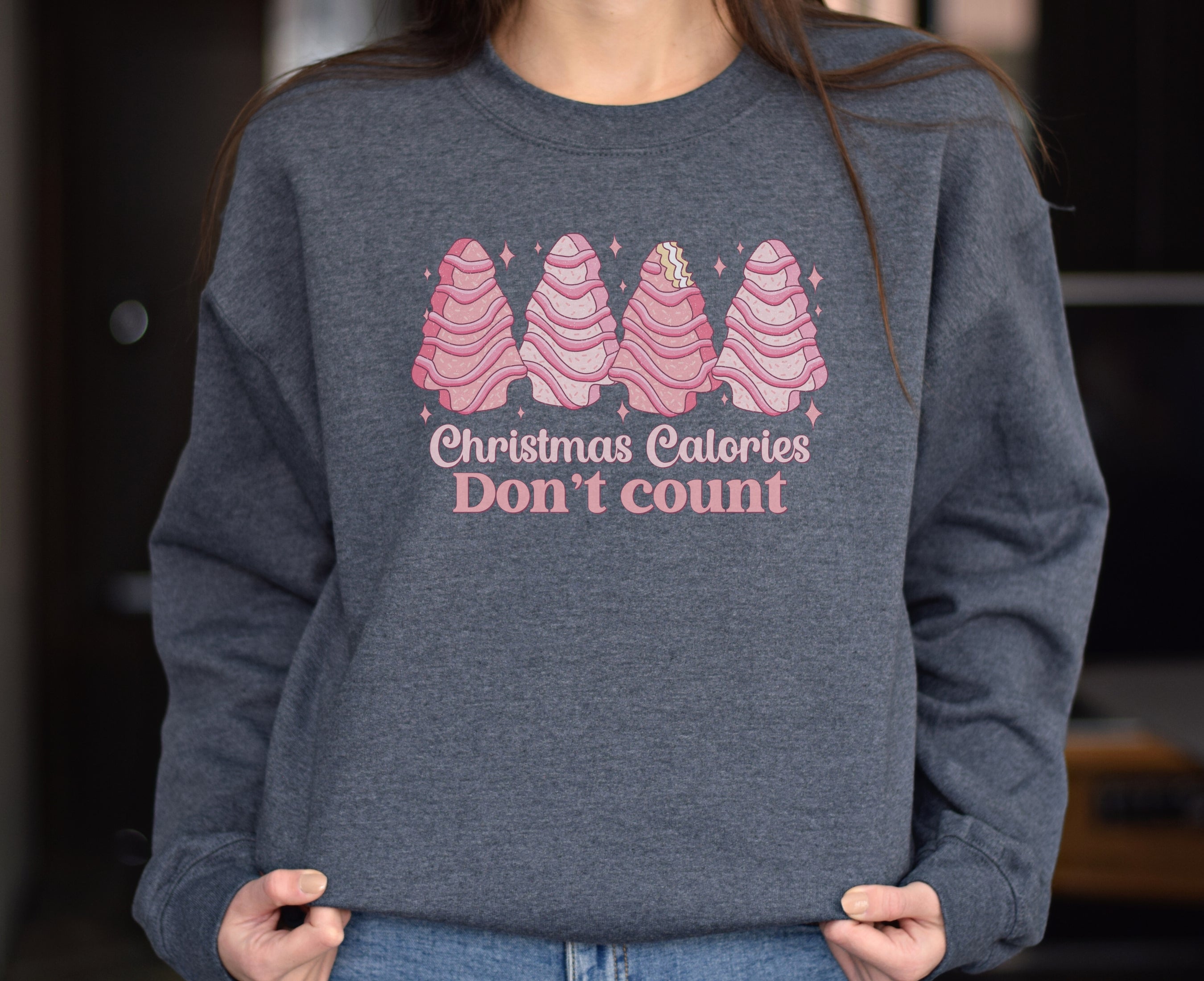 Girl wearing dark grey heather sweatshirt with pink Christmas tree cakes on it