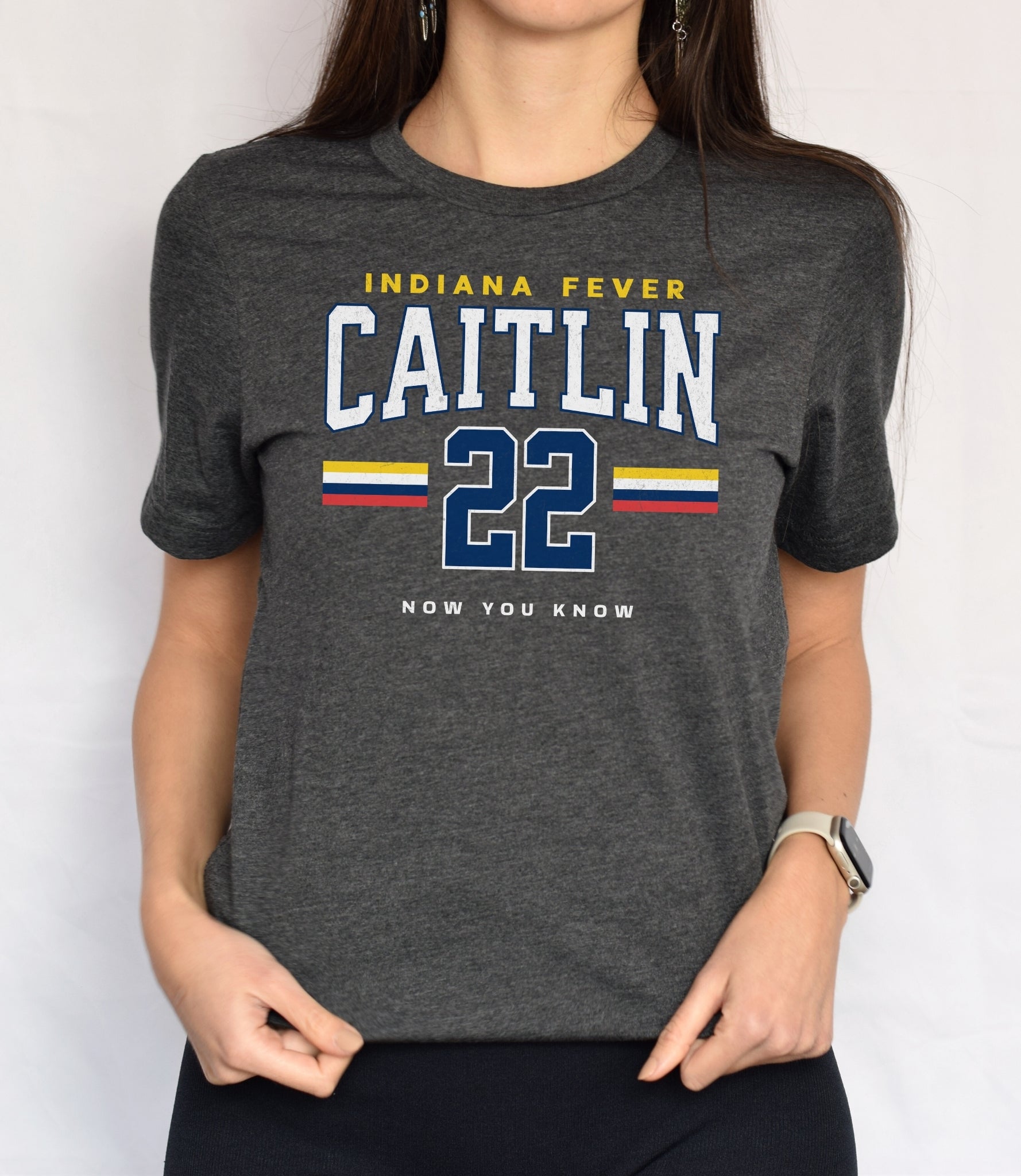 Person wearing a dark gray t-shirt with 'Indiana Fever Caitlin 22 Now You Know' text in front of white background