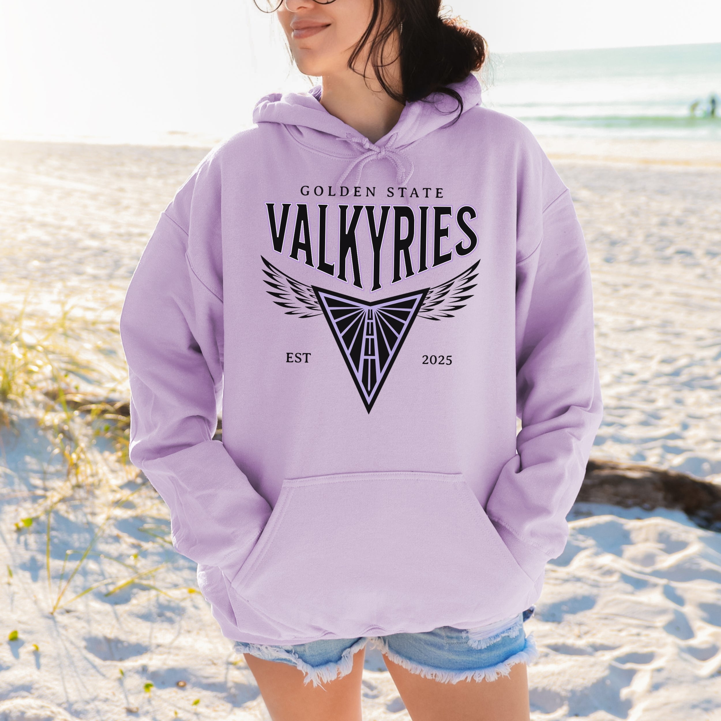 Person wearing a lavender hoodie with 'Golden State Valkyries' text and design on a beach.