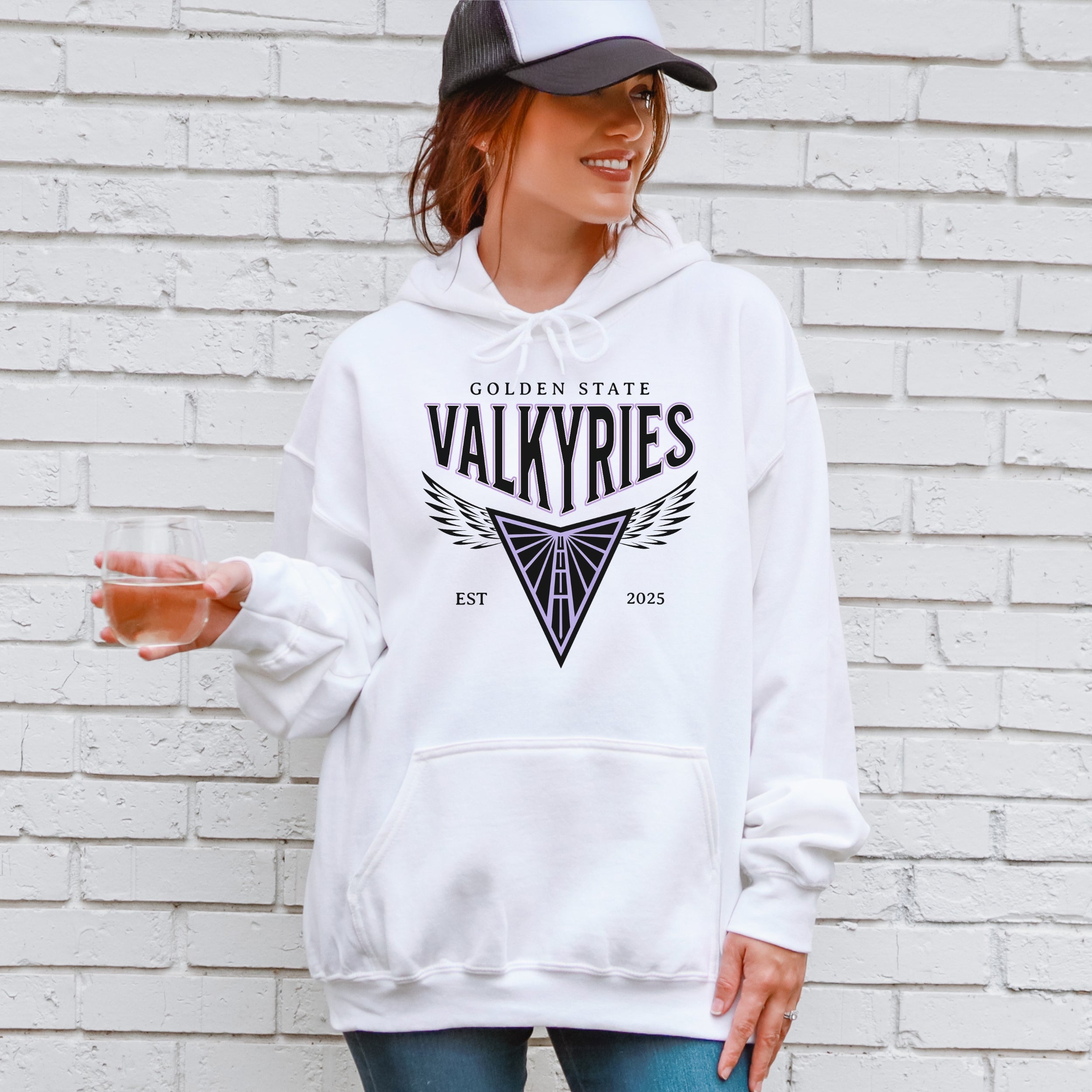 Person wearing a white hoodie with 'Golden State Valkyries' logo against a brick wall.