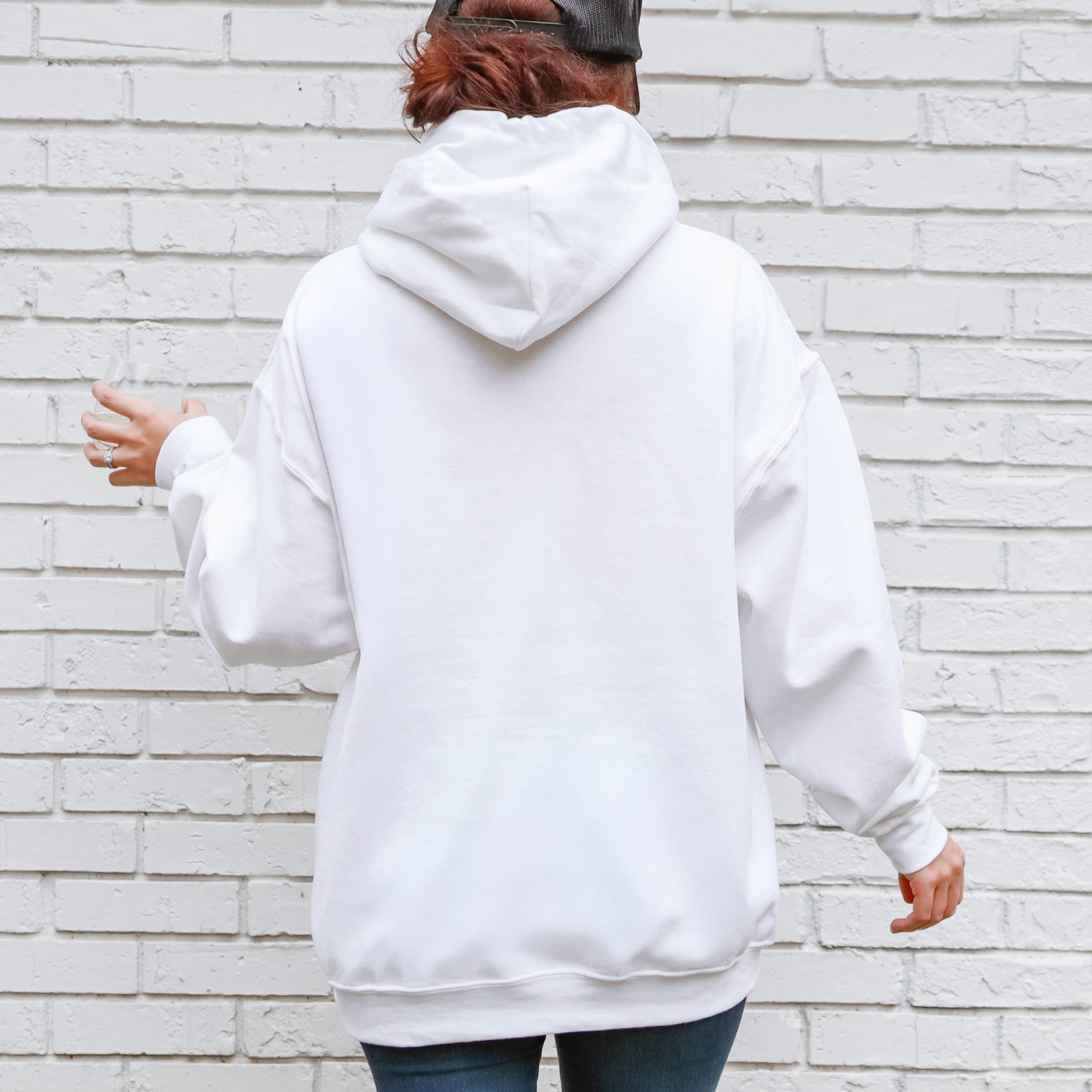 Person wearing a white hoodie standing against a light brick wall.
